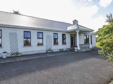 The front exterior of a single-story house with several windows and potted plants near the entrance at Belladrihid Cottage Ballysadare near Sligo County Sligo