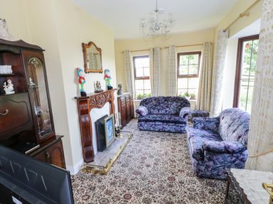 A living room with two floral patterned sofas a fireplace wooden cabinets and windows with curtains at Belladrihid Cottage Ballysadare near Sligo County Sligo