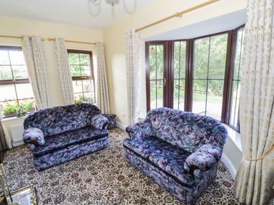 A room with two floral patterned sofas near windows with curtains and a patterned carpet at Belladrihid Cottage Ballysadare near Sligo County Sligo