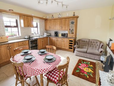A kitchen with wooden cabinets a round dining table with red and white tablecloth and sofa at Belladrihid Cottage Ballysadare near Sligo County Sligo