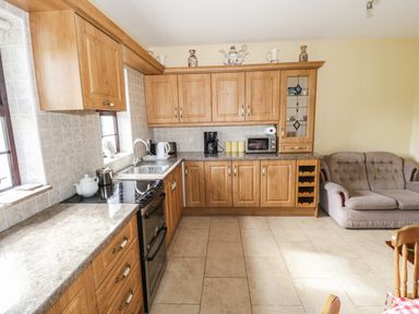 A kitchen with wooden cabinets countertop appliances a sofa and part of a wooden chair at Belladrihid Cottage Ballysadare near Sligo County Sligo