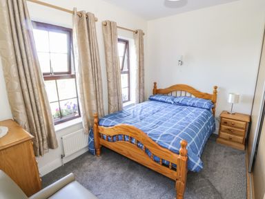 A bedroom with a wooden bed with blue checkered bedding two windows with beige curtains and wooden furniture at Belladrihid Cottage in Ballysadare near Sligo County Sligo