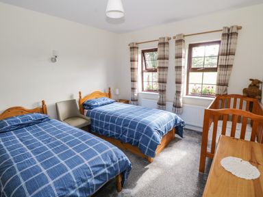 A bedroom with two single beds covered in blue checkered bedding a crib a wooden dresser and two windows with curtains at Belladrihid Cottage in Ballysadare near Sligo County Sligo