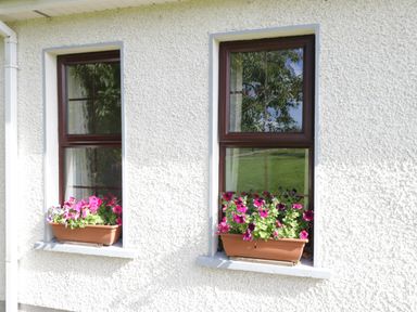 Two windows with brown frames and flower boxes with pink and purple flowers on the exterior wall of a white building at Belladrihid Cottage Ballysadare near Sligo County Sligo