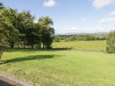 A grassy lawn with trees and a fence overlooking fields with distant hills at Belladrihid Cottage Ballysadare near Sligo County Sligo