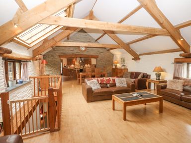 A living area with exposed wooden beams leather sofas wooden coffee table and dining table in a barn conversion at Cowslip Barn in Cornworthy near Dittisham