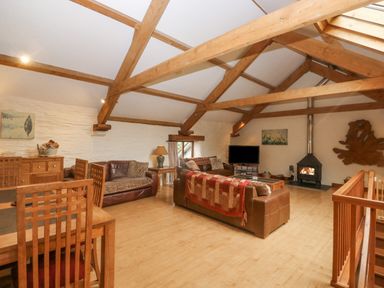 A living room with exposed wooden beams wooden dining chairs sofas a fireplace and a television at Cowslip Barn Cornworthy near Dittisham