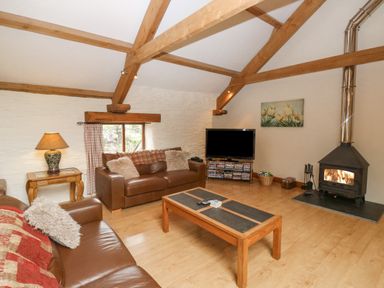 A living room with wooden beams a fireplace two brown leather sofas a wooden coffee table and a television at Cowslip Barn in Cornworthy near Dittisham