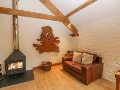 A living room with a wood burning stove a brown leather sofa and a wooden wall decoration at Cowslip Barn in Cornworthy near Dittisham