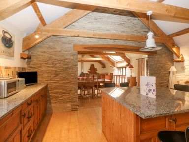 A kitchen with wooden cabinets granite countertops exposed wooden beams and a dining area with wooden chairs at Cowslip Barn in Cornworthy near Dittisham