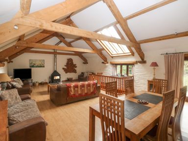 A living room and dining area with wooden beams and a wood burning stove at Cowslip Barn in Cornworthy near Dittisham