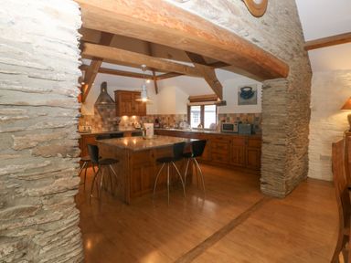 A kitchen with a central island and stools under wooden beams at Cowslip Barn in Cornworthy near Dittisham