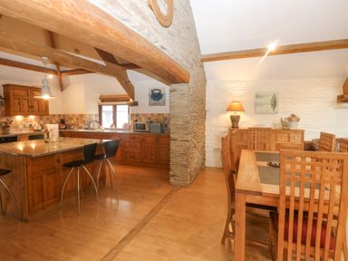 An open kitchen and dining area with wooden cabinets chairs and a stone pillar at Cowslip Barn in Cornworthy near Dittisham