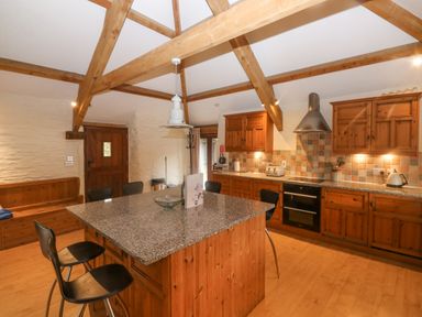 A kitchen with wooden cabinets a granite island and exposed wooden beams at Cowslip Barn in Cornworthy near Dittisham