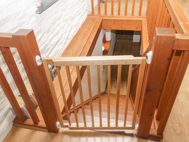 A wooden baby gate at the top of a wooden staircase with wooden railings and a white textured wall at Cowslip Barn in Cornworthy near Dittisham