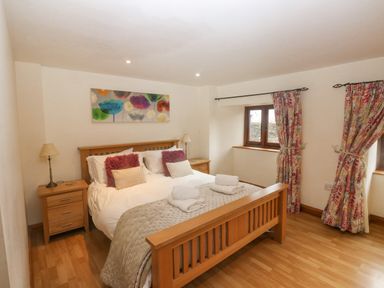 A bedroom with a double bed bedside tables lamps and floral curtains at Cowslip Barn in Cornworthy near Dittisham