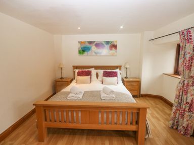 A bedroom with a wooden double bed two bedside tables with lamps and floral curtains at Cowslip Barn in Cornworthy near Dittisham