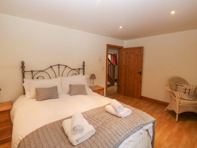 A bedroom with a double bed two bedside tables a wicker chair and an open wooden door at Cowslip Barn in Cornworthy near Dittisham