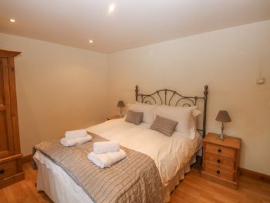 A bedroom with a double bed two bedside tables lamps and a wooden wardrobe at Cowslip Barn in Cornworthy near Dittisham