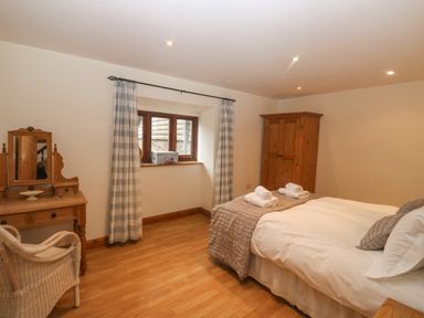 A bedroom with a double bed two rolled towels wooden wardrobe vanity table chair and window with curtains at Cowslip Barn in Cornworthy near Dittisham