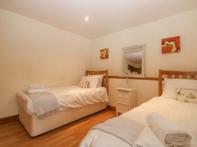 A bedroom with two single beds a white nightstand a lamp and a wall mirror at Cowslip Barn in Cornworthy near Dittisham