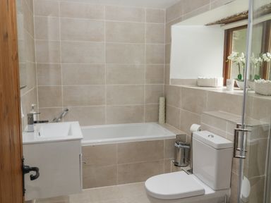 A bathroom with a bathtub a toilet a sink with faucet and a window with flowers at Cowslip Barn in Cornworthy near Dittisham