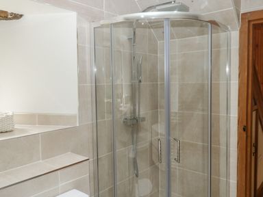 A bathroom with a glass corner shower enclosure and beige tiled walls at Cowslip Barn in Cornworthy near Dittisham