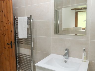 A bathroom with a wooden door chrome towel rack with white towel white sink and a mirror at Cowslip Barn in Cornworthy near Dittisham