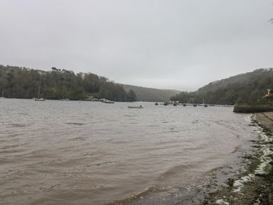 A shoreline with water, boats, and hills in the background at Cowslip Barn in Cornworthy near Dittisham
