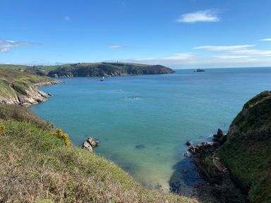 A coastal landscape with blue sea water surrounded by rocky cliffs and green hills at Cowslip Barn Cornworthy near Dittisham