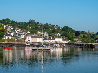 A coastal village with houses trees boats and a dock on calm water at Cowslip Barn in Cornworthy near Dittisham