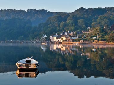 A small boat on calm water near a village with houses and hills at Cowslip Barn in Cornworthy near Dittisham