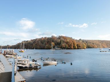 A river with boats docked and moored near a pier with a wooded hill in the background at Cowslip Barn in Cornworthy near Dittisham