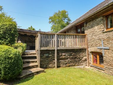 An outdoor area with stone steps leading to a wooden deck beside a stone building with windows at Cowslip Barn in Cornworthy near Dittisham