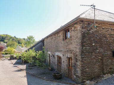 An exterior view of a stone barn with wooden windows and small trees along the side at Cowslip Barn in Cornworthy near Dittisham