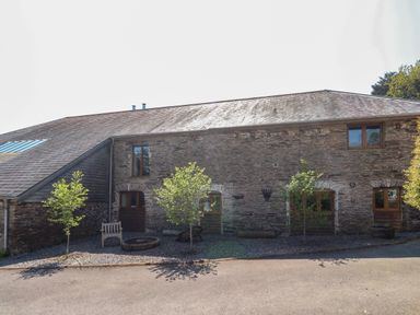 Stone barn with wooden window frames and doors small trees and a bench outside at Cowslip Barn in Cornworthy near Dittisham