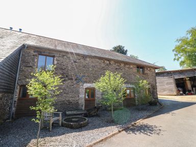 Stone building with wooden trim and windows next to a gravel path with small trees and wooden bench at Cowslip Barn Cornworthy near Dittisham