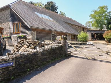 A stone barn with wooden gate and gravel driveway at Cowslip Barn in Cornworthy near Dittisham