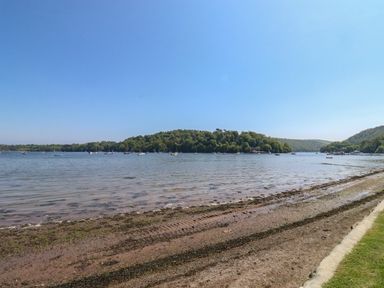 A shoreline with boats on water and a wooded hill in the background at Cowslip Barn in Cornworthy near Dittisham