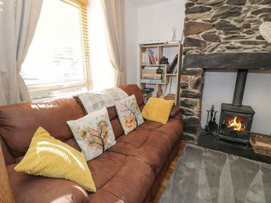 A living room with a brown sofa with decorative cushions next to a stone fireplace with a wood stove at Snowdon View in Llanberis