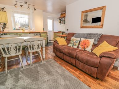 A kitchen and living area with a brown sofa and dining table with chairs at Snowdon View in Llanberis