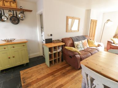 A living room with a brown sofa, wooden dining table, green cabinet, pots hanging on wall, and wooden floor at Snowdon View Llanberis