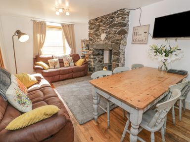 A living room with two brown sofas a wooden dining table with chairs a stone fireplace and a wall-mounted television at Snowdon View in Llanberis