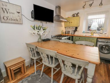 A kitchen with a wooden dining table and chairs a mounted television and green cabinets at Snowdon View in Llanberis