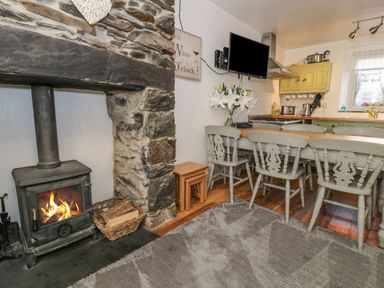A kitchen dining area with a wood burning stove and stone wall at Snowdon View in Llanberis