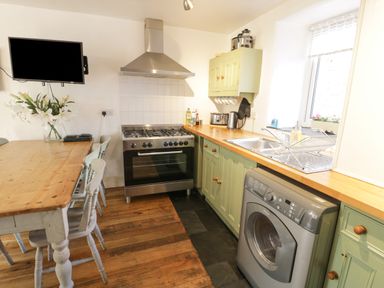 A kitchen with a wooden dining table and chairs a stove washing machine and green cabinets at Snowdon View in Llanberis