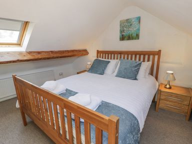A bedroom with a wooden bed frame white bedding blue cushions bedside tables with lamps and a skylight window at Snowdon View in Llanberis