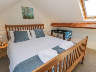 A bedroom with a wooden bed frame white bedding blue pillows bedside tables lamps a painting above the bed and a skylight window at Snowdon View in Llanberis