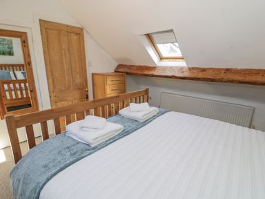 A bedroom with a wooden bed frame folded towels a chest of drawers and a skylight window at Snowdon View in Llanberis