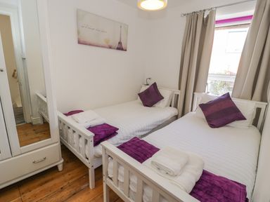A bedroom with two single beds purple pillows and blankets white wardrobe and wooden floor at Snowdon View in Llanberis